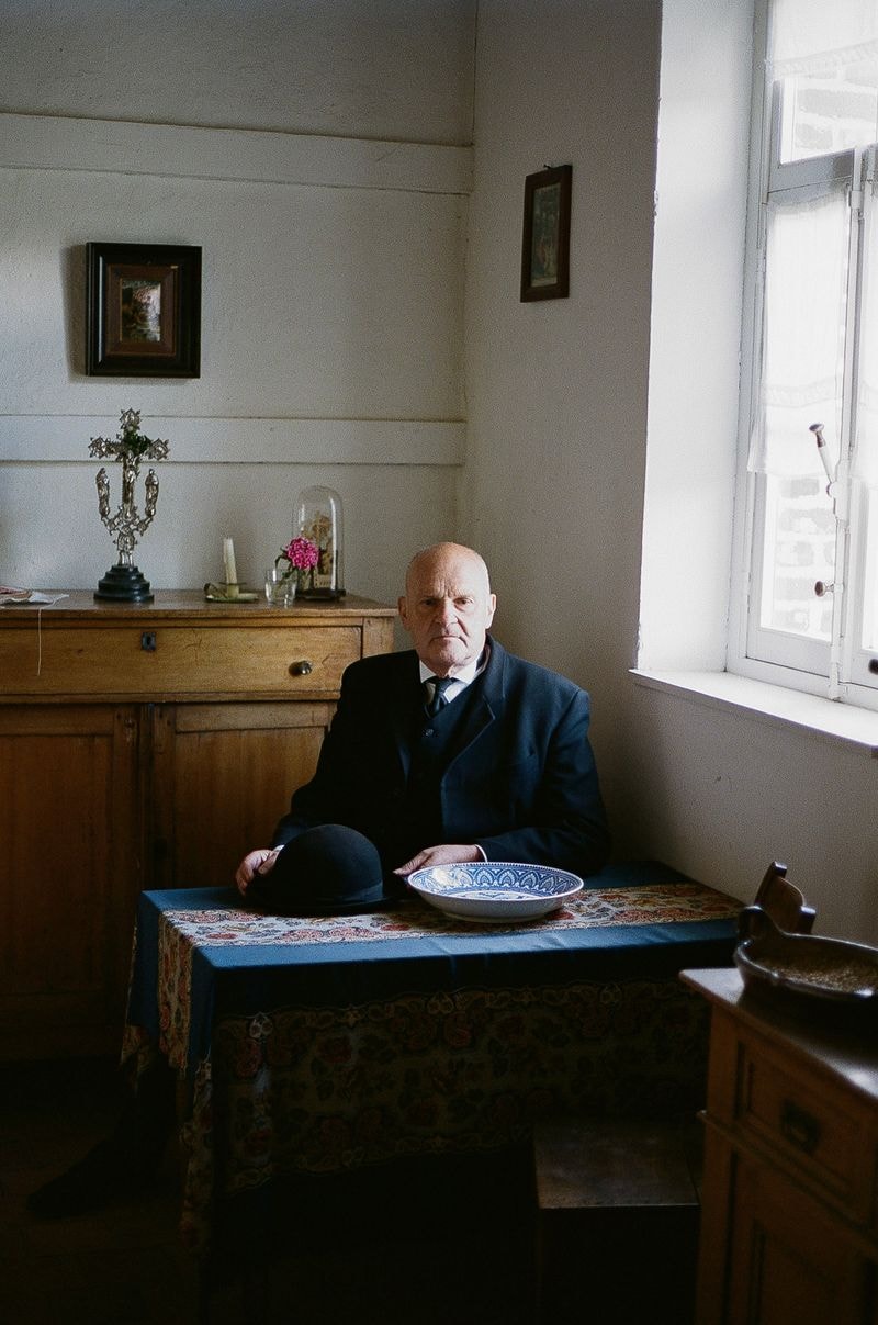 Man zit aan tafel in Genk Bokrijk met hoedje op tafel in ouderwets interieur, kijkt dromerig en intens
