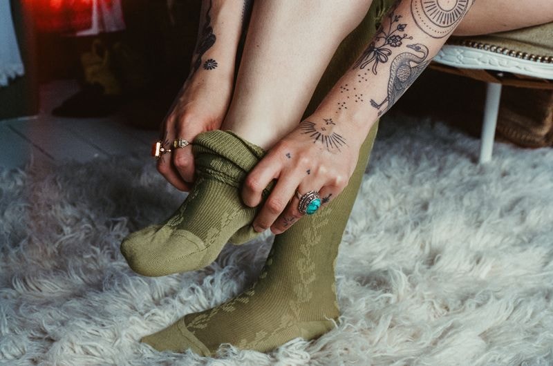 Jonge vrouw trekt sokken aan in artistiek atelier in Amersfoort, met kunstmaterialen op de achtergrond