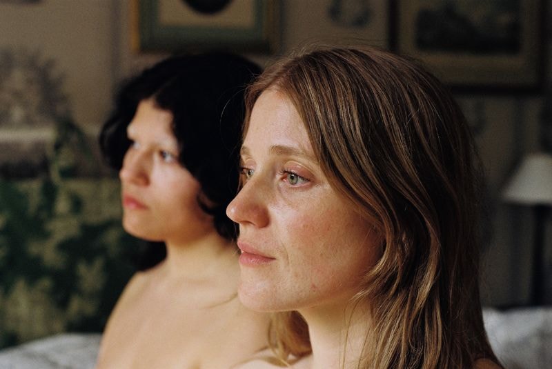 Twee vrouwen, één blond en één brunette, liggend op bed in Frans château, met dromerige blikken