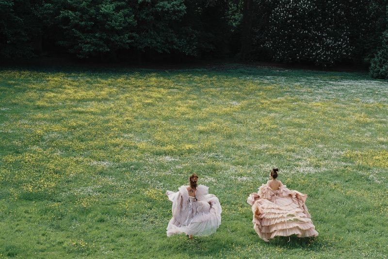 Twee dames rennen over groene weide, gekleed in grote prinsesachtige jurken