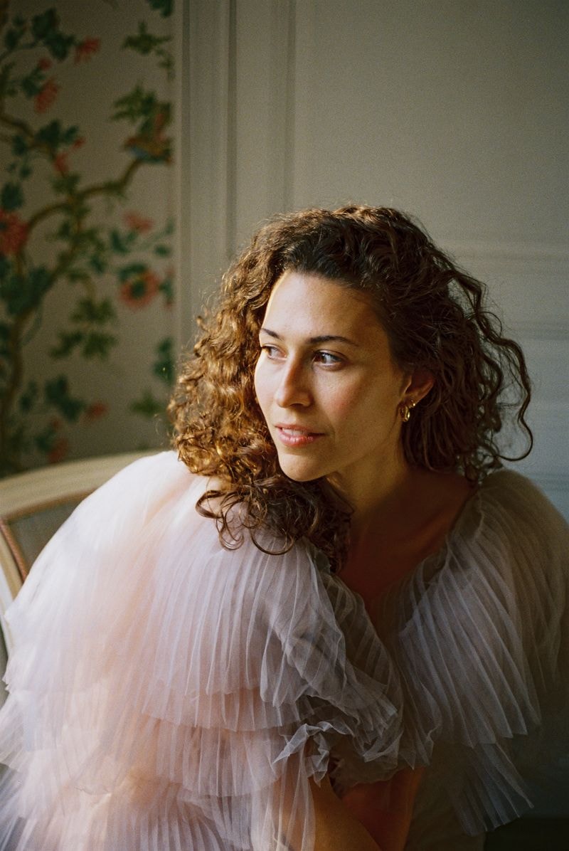 Meisje in elegante jurk kijkt uit het raam van een klassiek Frans château, met zacht invallend daglicht en uitzicht op de tuin