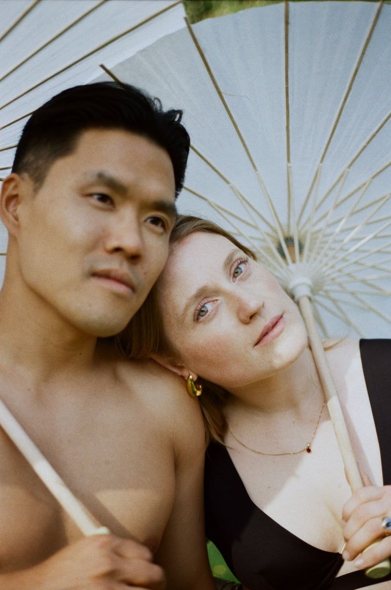 Koppel onder witte paraplu in Frankrijk, zij kijkt dromerig in camera, hij kijkt weg