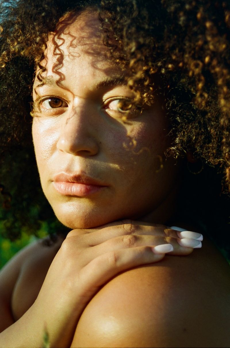 Meisje met krullend haar en witte nagels kijkt intens in camera in Utrechts veld