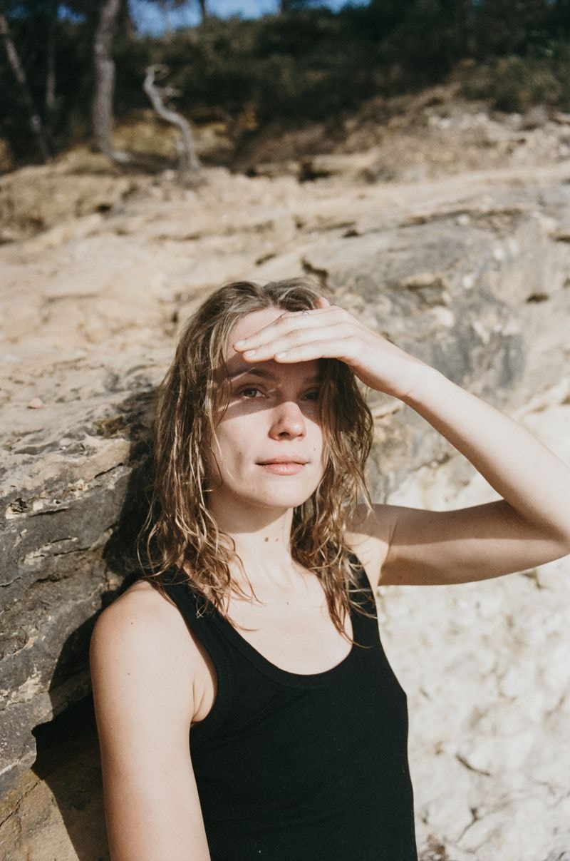 Jong meisje beschermt haar ogen tegen zonlicht op een zonnig Spaans strand, met rotsen op de achtergrond