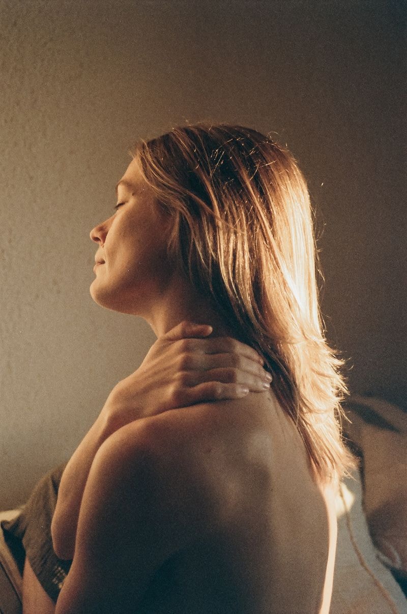 Meisje met hand op schouder liggend op bed in Sitges, gefotografeerd van zijkant in ochtendzon