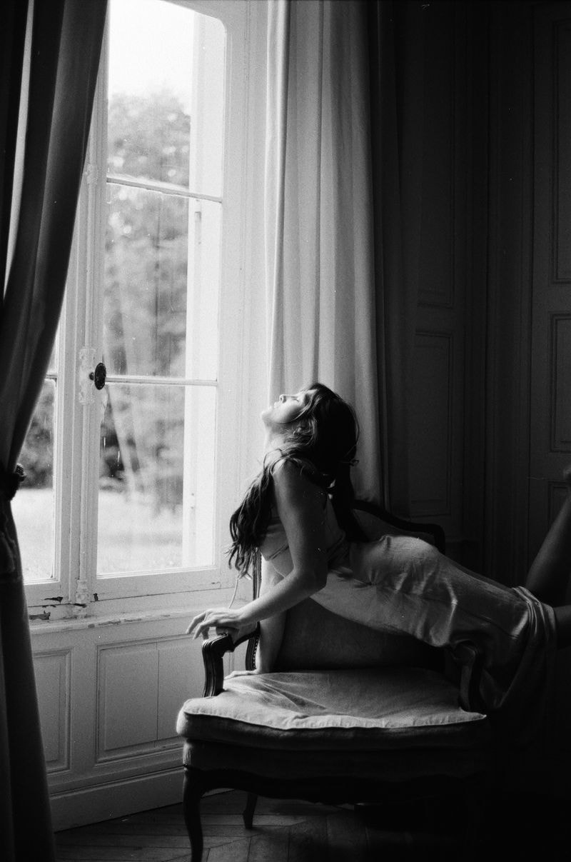 Meisje leunt sierlijk op een stoel, met gesloten ogen en een vloeiende beweging in haar lichaam, wat een gevoel van rust en elegantie uitstraalt