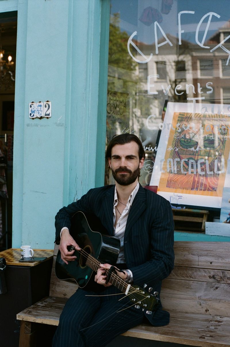 Man zittend met gitaar op bank voor koffiecafé op Oudegracht in Utrecht